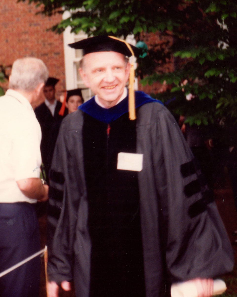 A young, smiling John Gainer wearing academic regalia on UVA's Grounds.