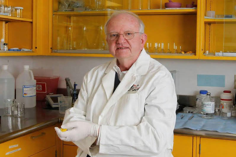 John Gainer, wearing latex gloves and a white lab coat, poses in his chemical engineering lab at UVA.
