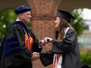 Chair Richard Kent presents a student with her diploma