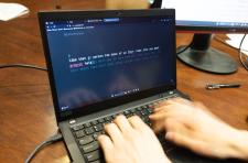 Close up of a laptop computer with writing on the screen and hands on the keyboard.