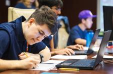UVA students seated around a conference room table covered with computers, computer monitors, and paper and pencils, work intently during the qualifying round  of the Mid-Atlantic Collegiate Competition.
