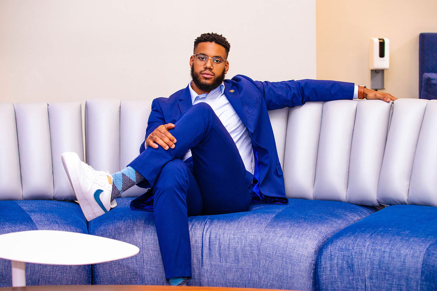 A young man in a blue suit posing for a photo on a white and blue couch.