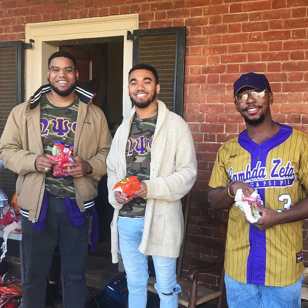Three young, smiling black men pose in front of rooms on UVA's historic Lawn.