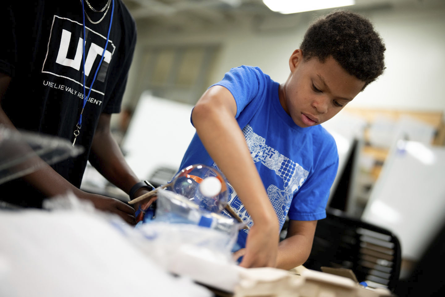 A students tapes together materials on his team's vehicle.