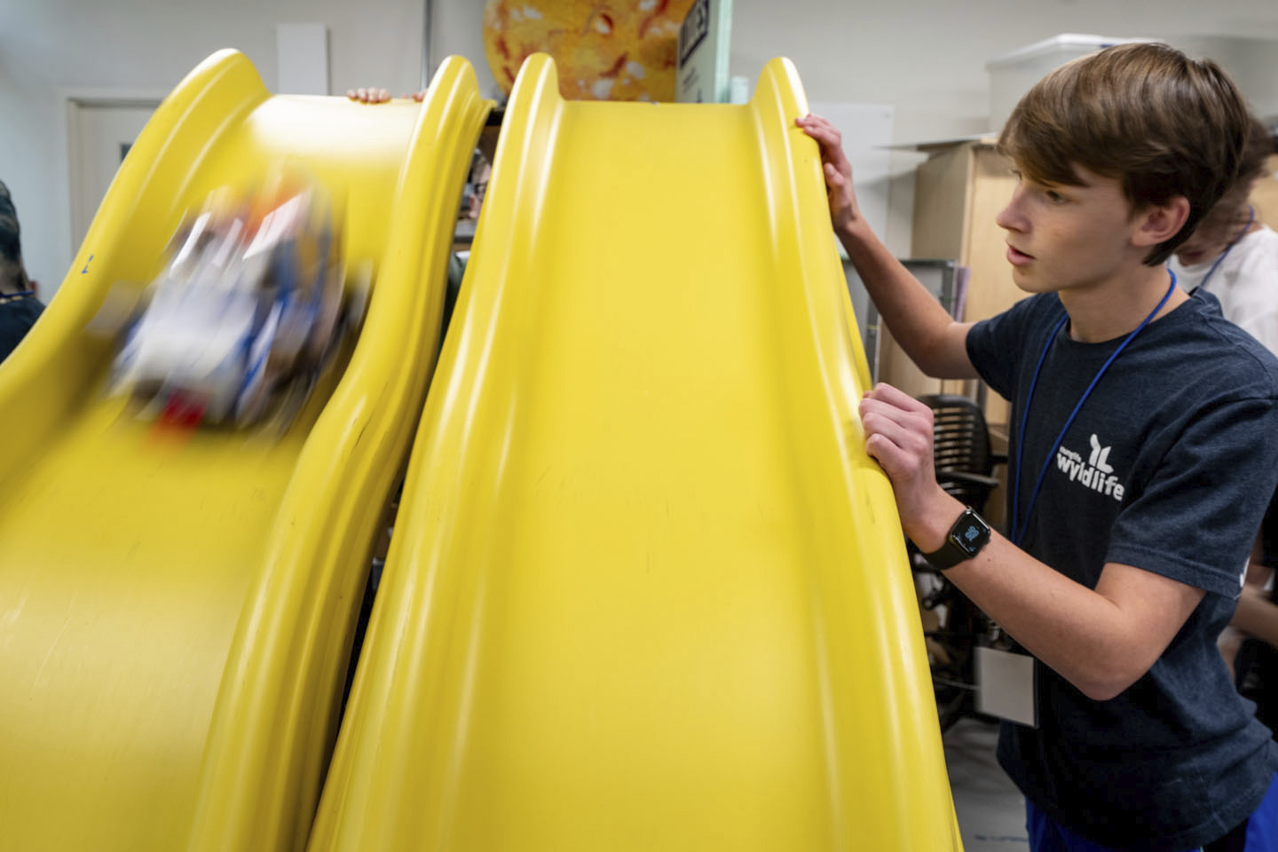 A student watches beside one slide as a vehicle goes down another.