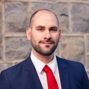 Image of a man wearing a red tie and blue jacket smiling