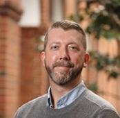 Image of man in grey sweater smiling outside