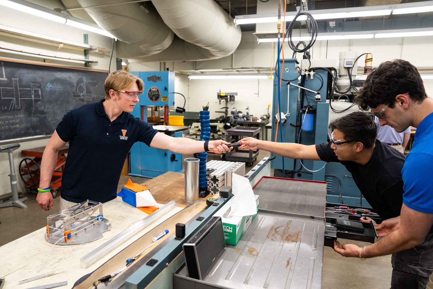 A student passes a screwdriver to be used on HEDGE, the components of which are pictured to the left.