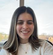 Image of woman in cream colored sweater standing in front of a window smiling