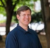 man in navy blue collared shirt smiling outside under trees