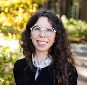 Image of woman in black sweater wearing glasses, smiling outside