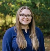 woman wearing blue shirt and glasses with long hair smiling outside