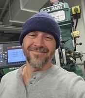 Image of man wearing grey shirt and blue hat in mechanical room smiling
