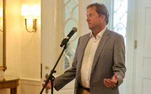 Scott Acton speaking at a mic and using his arms to help express his point.