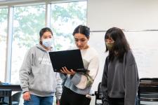 Three students work together, the one in the center holding a laptop