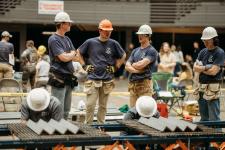 Three students in hardhats consult as weights are added.